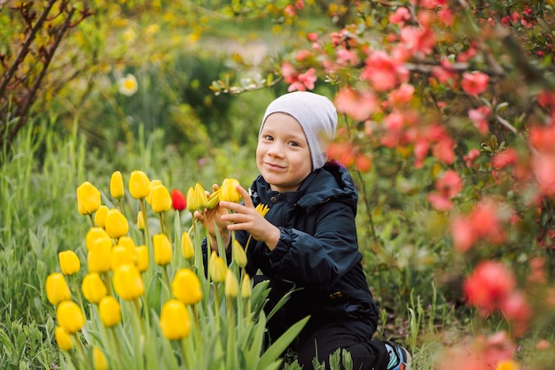 niño pequeño se sienta en un claro entre flores tulipanes