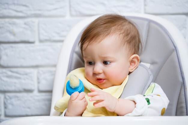 Un niño pequeño se sienta en una silla alta y come frutas a través de la red. Nibbler para alimentar a los bebés