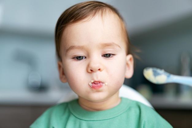 Niño pequeño se sienta en una silla y come con cuchara