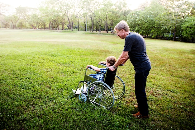 Niño pequeño en silla de ruedas con el abuelo en el parque al aire libre