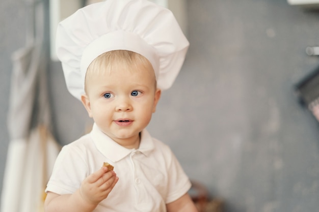 Un niño pequeño con sombrero de chef en la cocina sentado en la mesa y comer