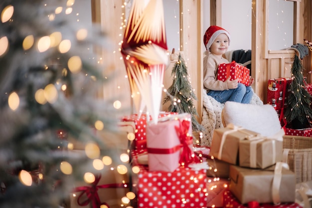 Niño pequeño con sombrero de santa jugando en su habitación infantil decorada para las vacaciones de navidad