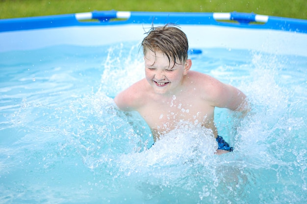 Un niño pequeño, sonriendo y cerrando los ojos, chapotea en la piscina con agua limpia y tibia en un sol