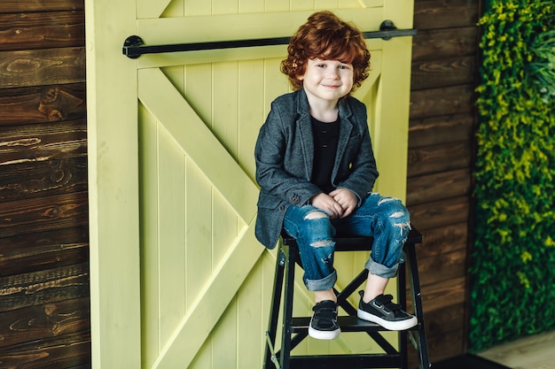 Niño pequeño sonriente en los vaqueros rasgados que se sientan en escalera y que parecen relajados