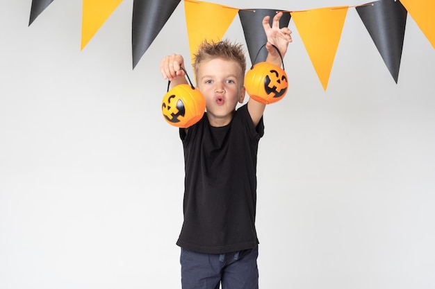 Un niño pequeño sosteniendo una canasta para golosinas asusta sobre un fondo blanco con una guirnalda Children's Halloween Trick or treat