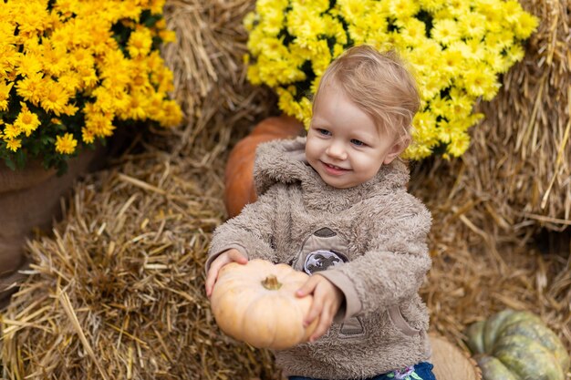 Foto un niño pequeño sostiene una calabaza en sus manos sobre un fondo de heno.