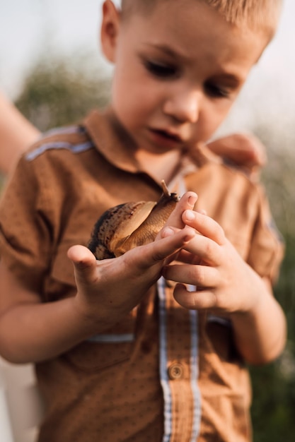 Un niño pequeño sostiene un caracol en sus manos y lo examina cuidadosamente