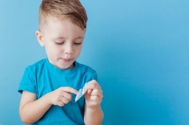 Foto un niño pequeño sostiene en su palma un puñado de píldoras sobre fondo azul.