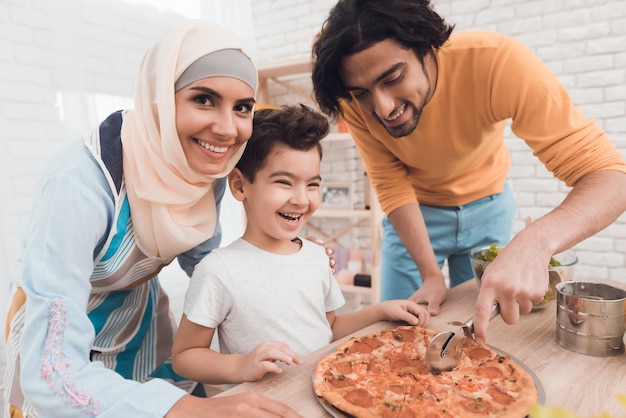 Un niño pequeño con su padre está cortando pizza.