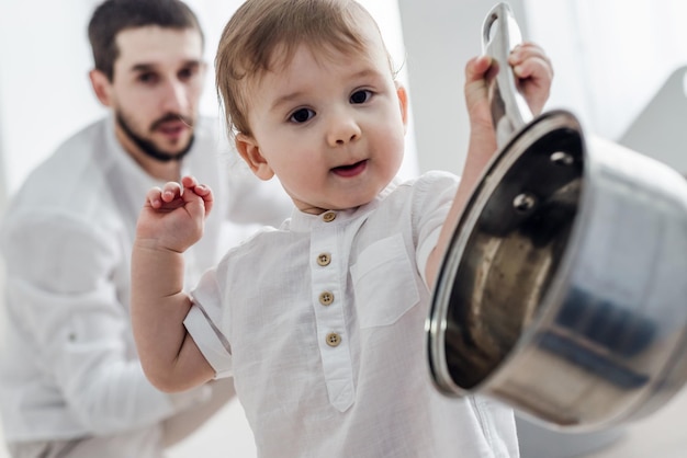 Niño pequeño con su padre juega con utensilios de cocina El niño muestra la sartén a la cámara