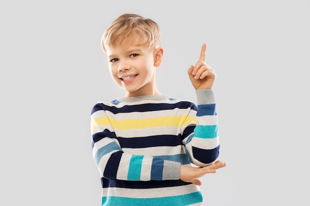 Foto niño pequeño con un suéter a rayas señalando con el dedo hacia arriba