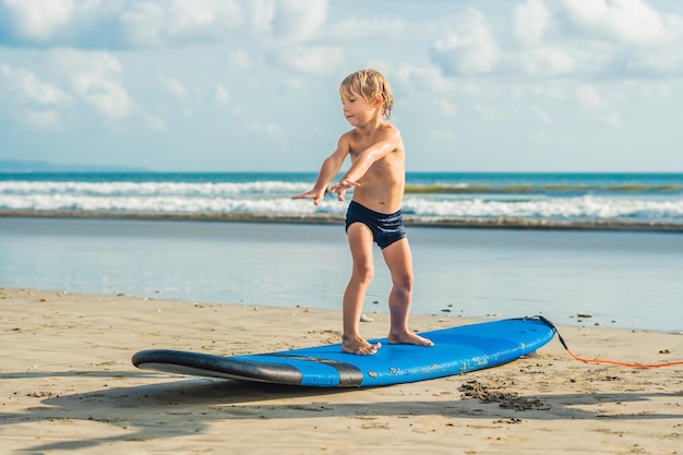 Niño pequeño surfeando en una playa tropical Niño en una tabla de surf en las olas del océano Deportes acuáticos activos para niños Niño nadando con surf Lección de surf para niños