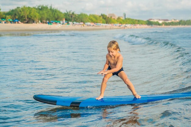 Niño pequeño surfeando en una playa tropical Niño en una tabla de surf en las olas del océano Deportes acuáticos activos para niños Niño nadando con surf Lección de surf para niños