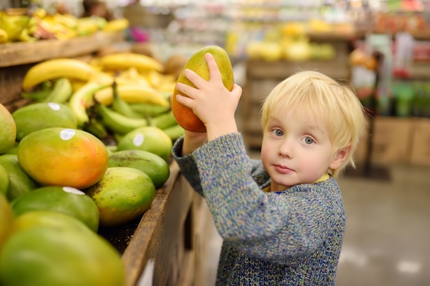 Niño pequeño en una tienda de alimentos o en un supermercado eligiendo mango orgánico fresco