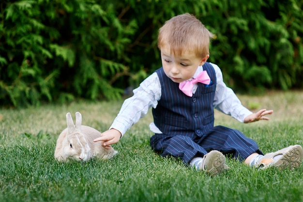 Niño pequeño en un traje jugando con un conejo en la hierba