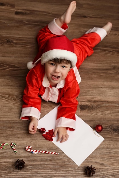 Niño pequeño en un traje de Santa Claus escribiendo una carta con deseos para el año nuevo