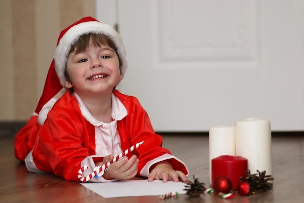 Niño pequeño en un traje de Santa Claus escribiendo una carta con deseos