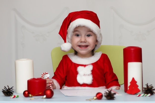 Niño pequeño en un traje de Santa Claus escribiendo una carta con deseos