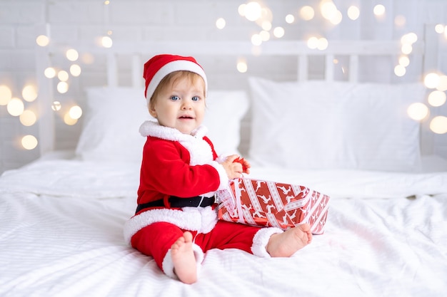 Niño pequeño en traje de santa sosteniendo un regalo de Navidad sentado sobre un fondo blanco año nuevo