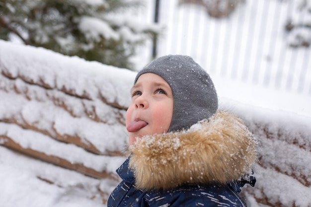 un niño pequeño trata de atrapar copos de nieve con la lengua en el invierno en la calle Se está divirtiendo