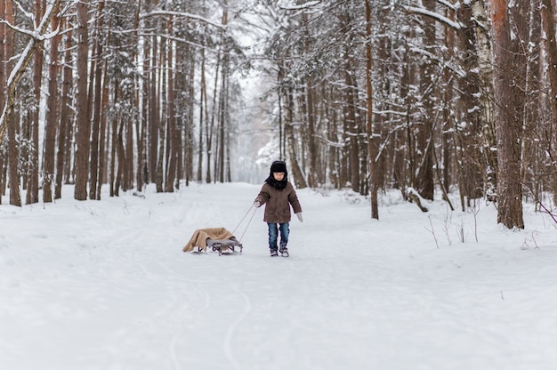 Niño pequeño con trineo en bosque de invierno