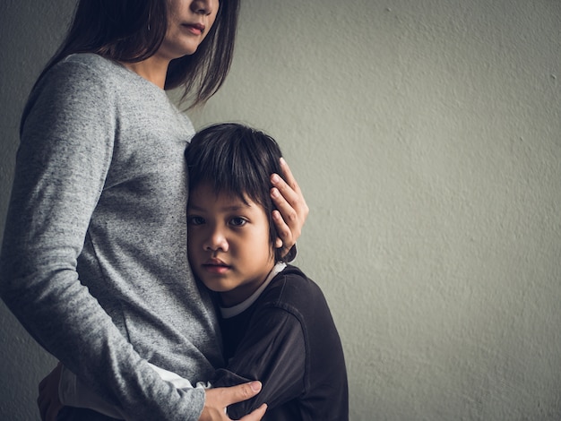 Niño pequeño triste abrazado por su madre en casa. amor, concepto de familia.