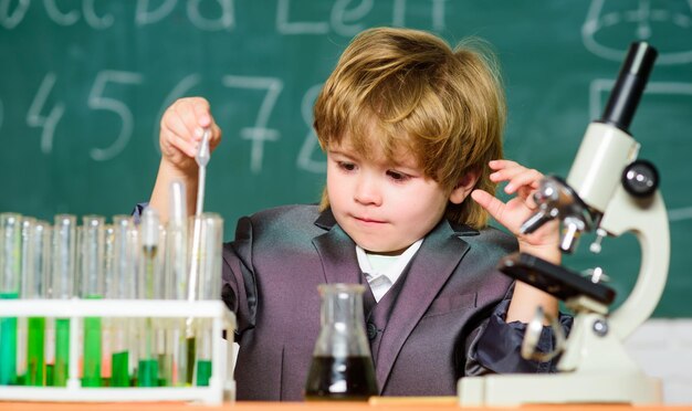 Niño pequeño usando microscopio en tubos de prueba de lección con líquido para investigación aprender para el futuro Resultado de ciencia biológica Concepto médico Pequeño niño genio niño pequeño estudio química