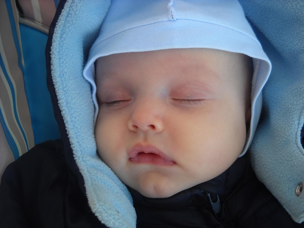 Un niño pequeño vestido de azul duerme en un cochecito durante un día de caminata. Se le pone al niño un gorro fino de algodón y un mono azul.