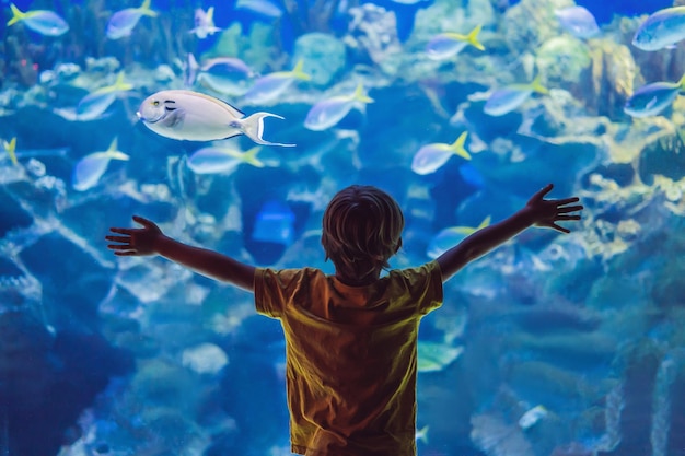 Niño pequeño viendo el cardumen de peces nadando en el oceanario niños disfrutando de la vida submarina en el acuario