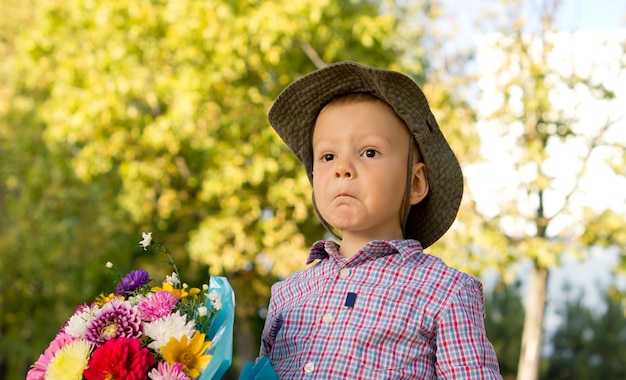 Niño perplejo tirando de una expresión divertida sosteniendo un ramo de flores para su madre