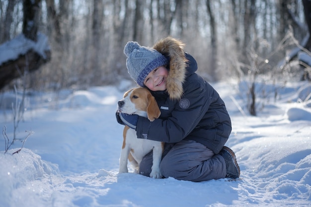 Niño y perro Beagle caminando y jugando en el bosque cubierto de nieve de invierno en un día soleado helado