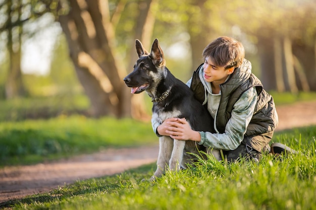 Un niño con un perro camina en el parque en una soleada tarde de primavera sentado en el césped Amistad del hombre y el estilo de vida saludable de los animales