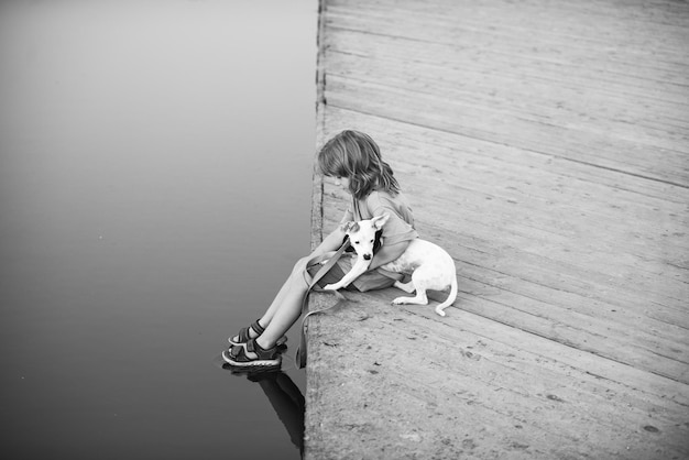 Niño con perro sentado en el parque cerca del agua