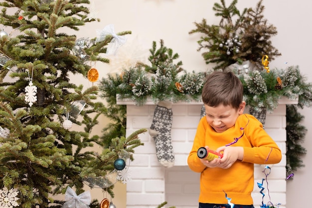Niño con petardo en las manos cerca del árbol de Navidad decorado y la chimenea Concepto de vacaciones acogedoras de invierno o año nuevo Fondo de Navidad con enfoque selectivo