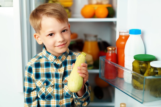 Niño de pie delante de la nevera abierta y eligiendo comida