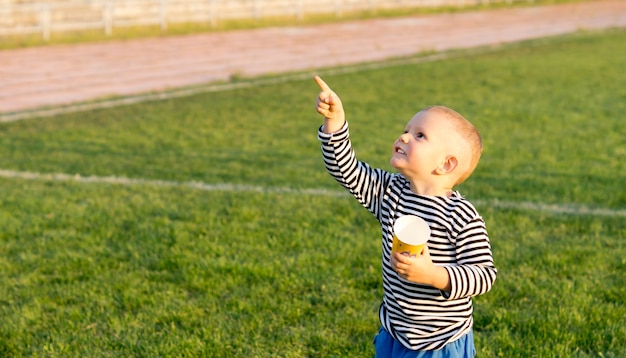 Niño de pie sobre un campo de juego verde con una taza en la mano apuntando al cielo