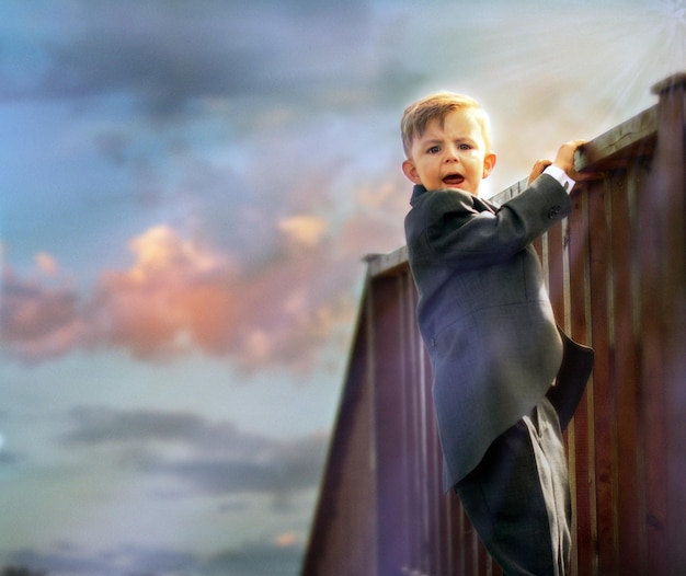 Foto niño de pie en una valla de madera contra el cielo