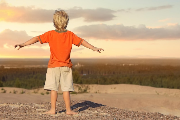 Niño de pie y viendo la puesta de sol en la montaña de arena