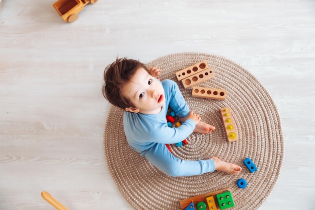 Un niño en pijama está sentado en el suelo de su habitación y jugando con un kit de construcción de madera juguetes naturales para niños el niño está jugando en su dormitorio