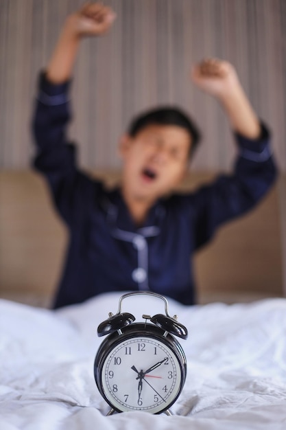 Foto un niño en pijama estirándose en la cama en casa por la mañana en una cama blanca con despertador