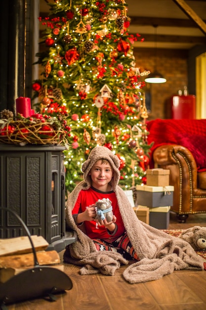 Un niño en pijama de Navidad se sienta cerca de un árbol de Navidad