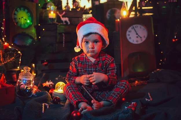 Un niño, con un pijama navideño a cuadros en un ambiente festivo de Año Nuevo. Foto en postal con luz de colores.