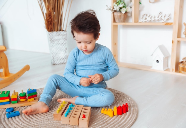 Foto un niño en pijama está sentado en el suelo de su habitación y jugando con un kit de construcción de madera juguetes naturales para niños el niño está jugando en su dormitorio