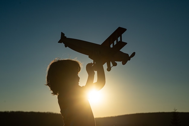 Niño piloto aviador con avión sueña con viajar. Sueños de niños. Niño en el fondo del cielo al atardecer.