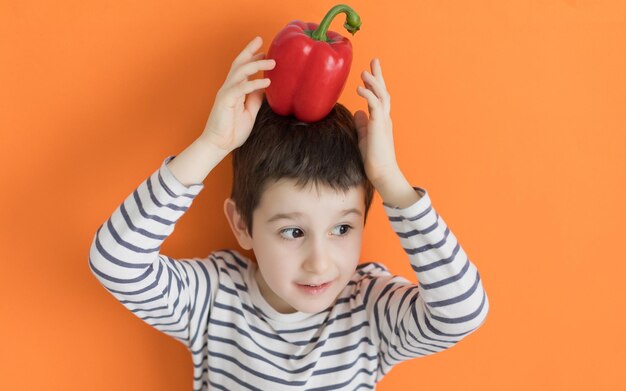Niño con pimiento rojo vegetal sobre un fondo naranja con espacio de copia Concepto de comida saludable mercado agrícola de verduras frescas