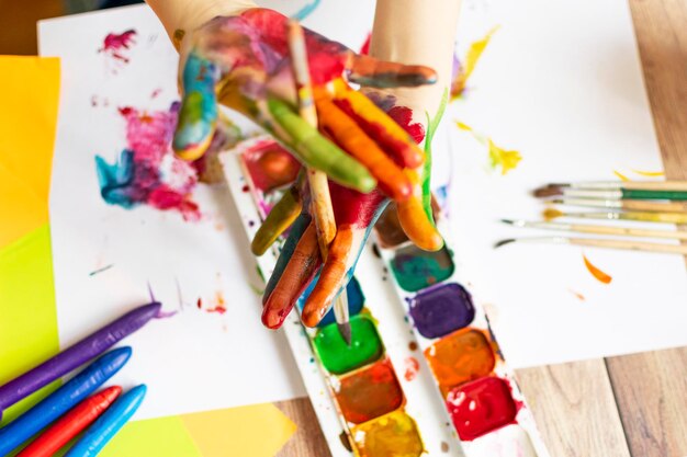 El niño pinta Palmas y manos de un niño en acuarela multicolor Pinceles de acuarela gouache de colores y pegatinas de crayones de cera Conjunto para dibujar creatividad y pasatiempos