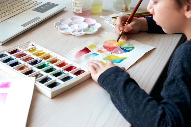 Niño pintando cuadros con pinturas de acuarela durante la lección de arte en línea