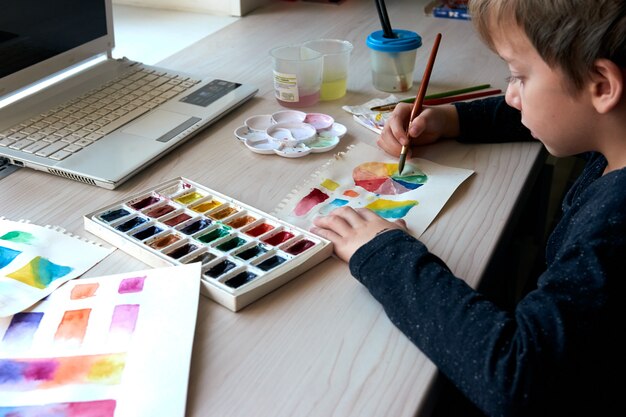 Niño pintando cuadros con pinturas de acuarela durante la lección de arte