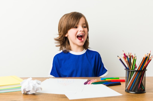 Niño pintando y haciendo los deberes en su escritorio gritando.