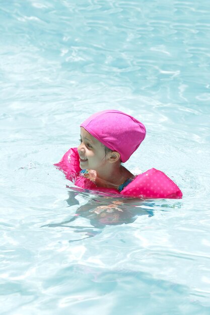 Niño en la piscina nadando con flotador rosa con agua azul